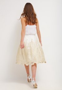 Witte rok met een scalloped zoom en gouden kant borduursel, gecombineerd met een witte camisole en zilveren hoge hakken sandalen.