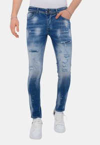 Blauwe denim jeans met een slim fit, met destructie details, lichte vervaging en verfspat accenten, gecombineerd met witte sneakers.