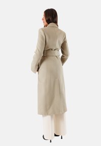 Cappotto in misto lana color cammello con vita cinturata, maniche lunghe e tasche laterali; presenta una linea dritta e rever a punta.