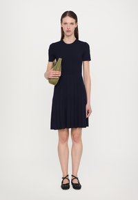Navy ribbed knit dress with short sleeves, pleated skirt, and solid color. Person holds a green suede clutch. Black shoes with polka dots.