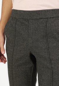 Grey tailored trousers made of textured fabric, featuring a fitted waist, side pockets, and subtle stitching details.