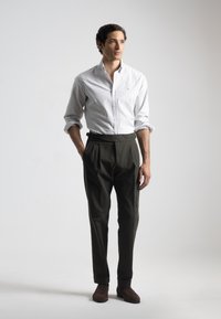 Camisa de botones a rayas blancas y gris claro con mangas enrolladas, combinada con pantalones de vestir verdes oscuros y botas de tobillo marrones.