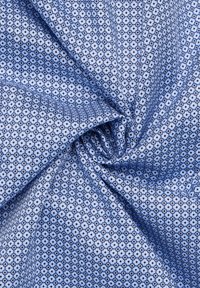 Blauw geweven stof met kleine hexagonale vormen in donkerblauw en wit tegen een lichtblauwe achtergrond. Zachte textuur, rimpelige uitstraling.
