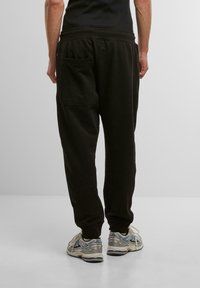Svarta joggerbyxor med avslappnad passform, med en bakficka och elastisk midja. Matchat med ljusgrå och blå sneakers.