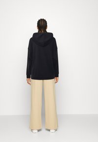 Felpa nera con cappuccio e vestibilità comoda, abbinata a pantaloni beige chiaro a gamba larga. Tessuto liscio; dettagli di design non visibili.