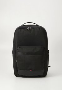 Musta nailonreppu, jossa kaksoisvetoketjut, etutasku ja vaakasuora nauha. Alareunassa pieni kolmen värin logo.