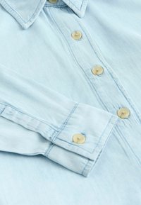 Lichtblauwe denimhemd met een klassieke kraag, knoopsluiting aan de voorkant en beige knopen met stiksel. Zachte textuur en casual ontwerp.