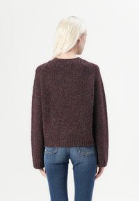 Pullover in magenta lavorato a maglia con finitura testurizzata, orlo a coste e spalle cadenti, abbinato a jeans blu aderenti.