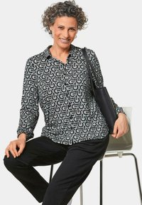 Zwart-wit gestippeld overhemd met lange mouwen en een button-down kraag, textuurstof en gerimpelde manchetten, gedragen met zwarte broek.
