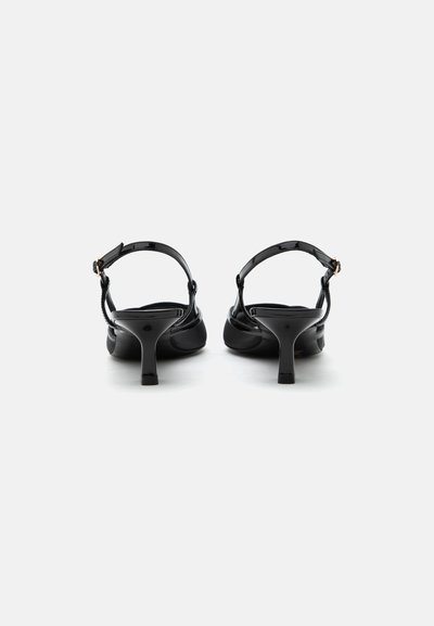 Talons slingback en cuir verni noir avec un petit talon fin et des brides ajustables à la cheville, vus de dos.
