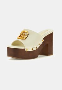 Mule con platform, realizzati in un materiale sintetico crema, con accessori in oro e tacco a blocco marrone texture. Presentano borchie decorative lungo la suola.