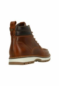 Botte en cuir marron avec un dos surélevé, un design à lacets et une semelle en caoutchouc blanche et marron. Avec œillets en métal et une languette d'aide à l'enfilage.