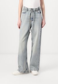 Light blue denim wide-leg jeans with a drawstring waist, front pockets, and a faded finish. Worn with white sneakers for contrast.