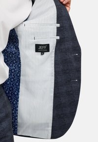 Wnętrze marynarki z trzema kieszeniami, białą, prążkowaną podszewką oraz niebieską tkaniną w wzory. Widoczna metka "JEFF URBAN TAILORING".