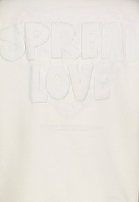 Witte sweatshirts met verhoogde, zachte letters die "SPREAD LOVE" spellen en een subtiel hartpatroon op de achtergrond, met een gestructureerde stof.