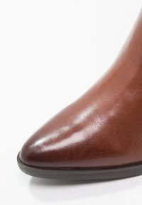 Gros plan d'une chaussure en cuir marron poli à bout pointu avec une semelle noire sur fond blanc.
