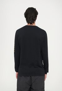 Must nägude seljaooga must pikkade varrukatega särk, milles on ümar kaelus ja sirge lõige. Vasakul varrukal on trükitud aktsendid. Pehme kangamaterjal.