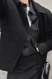 Črn volnen plašč z velikimi reverji preko temno črtaste srajce z gumbi. Obleka vključuje oprijet črn krilo in elegantno črno torbico.