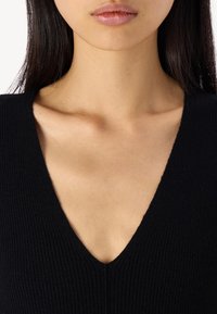 Svart ribbat stickad topp med djup V-ringning, med en kroppsnära design och slät textur. Minimalistisk stil, inga synliga mönster.