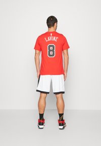 Rotes Sporttrikot mit schwarzer Beschriftung "LAVINE" und der Nummer "8" auf dem Rücken, kombiniert mit weißen Shorts und roten, schwarzen und goldenen Sneakers.