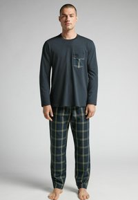 Navyblå långärmad topp med bröstficka, kombinerad med rutiga pyjamasbyxor med gröna och vita linjer på en mörk bakgrund.