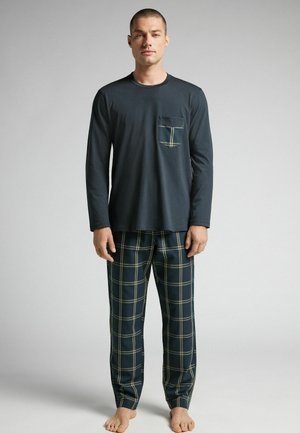 Haut à manches longues bleu marine avec une poche sur la poitrine, associé à un pantalon de pyjama à carreaux présentant des lignes vertes et blanches sur un fond sombre.