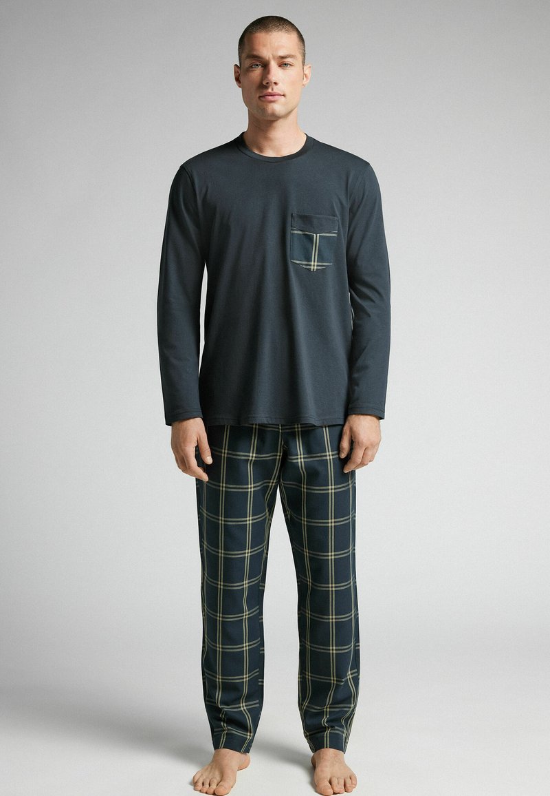 Navyblå långärmad topp med bröstficka, kombinerad med rutiga pyjamasbyxor med gröna och vita linjer på en mörk bakgrund.