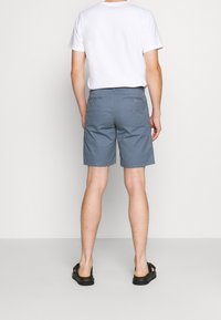 Shorts de color azul claro para hombre, con bolsillos laterales y bolsillos traseros con botón, fabricados con una tela suave, combinados con una camiseta blanca y sandalias negras.