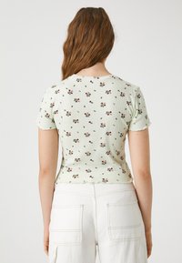 Jasnozielony prążkowany t-shirt z krótkimi rękawami, ozdobiony kwiatowym wzorem w odcieniach czerwieni i różu, z okrągłym dekoltem i falbanowym wykończeniem na dole.