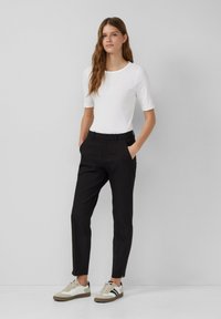 Witte ribbelige top met korte mouwen, zwarte aansluitende broek met zijzakken, en beige sneakers met zwarte strepen en textuuraccenten.