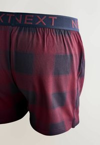 Męskie bokserki z miękkiej tkaniny, w bordowo-granatową kratę, z elastycznym paskiem w talii z napisem „NEXT” oraz luźnym krojem.