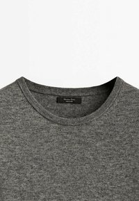 Pull gris en maille avec col rond côtelé et une petite étiquette noire à l'intérieur de l'encolure.