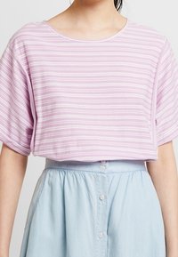 Ljuslila randig topp med korta dolmansärmar, rund halsringning och avslappnad passform. Matchas med en ljusblå skjortkjol.