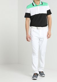 Polo à rayures noires, blanches et vertes avec col, associé à un pantalon blanc et des chaussures grises avec des accents orange. Coupe simple et sportive.