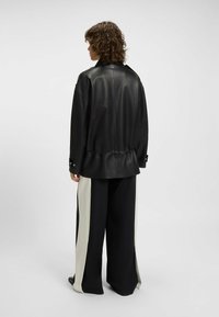 Black leather jacket with a cinched waist, long sleeves, and silver hardware; paired with wide black pants featuring cream side panels.
