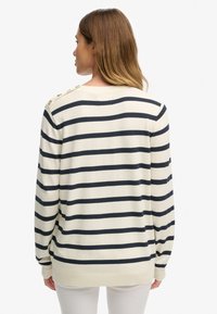 Jasnobeżowy sweter z granatowymi poziomymi paskami, z okrągłym dekoltem i detalem z trzema guzikami na ramieniu. Gładka faktura i długie rękawy.