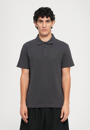 Dark gray polo shirt made of cotton blend, featuring a ribbed collar, two buttons, and a tonal logo patch on the left chest.