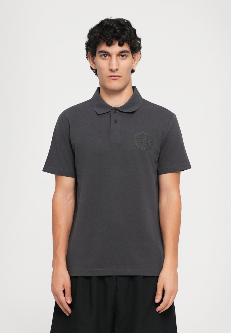 Mørkegrå polo-skjorte laget av bomullsblanding, med ribbestrikket krage, to knapper og en tonet logo-patch på venstre bryst.