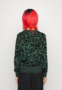 Pull vert et noir à motifs avec ourlet et poignets côtelés, doté d'un col rond et d'une coupe décontractée. Texture lisse.