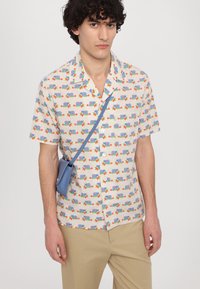 Kurze Ärmel Knopfhemd in Creme mit einem bunten Auto- und Blumenmuster. Kombinieren Sie es mit hellbeigen Hosen und einer blauen Umhängetasche.