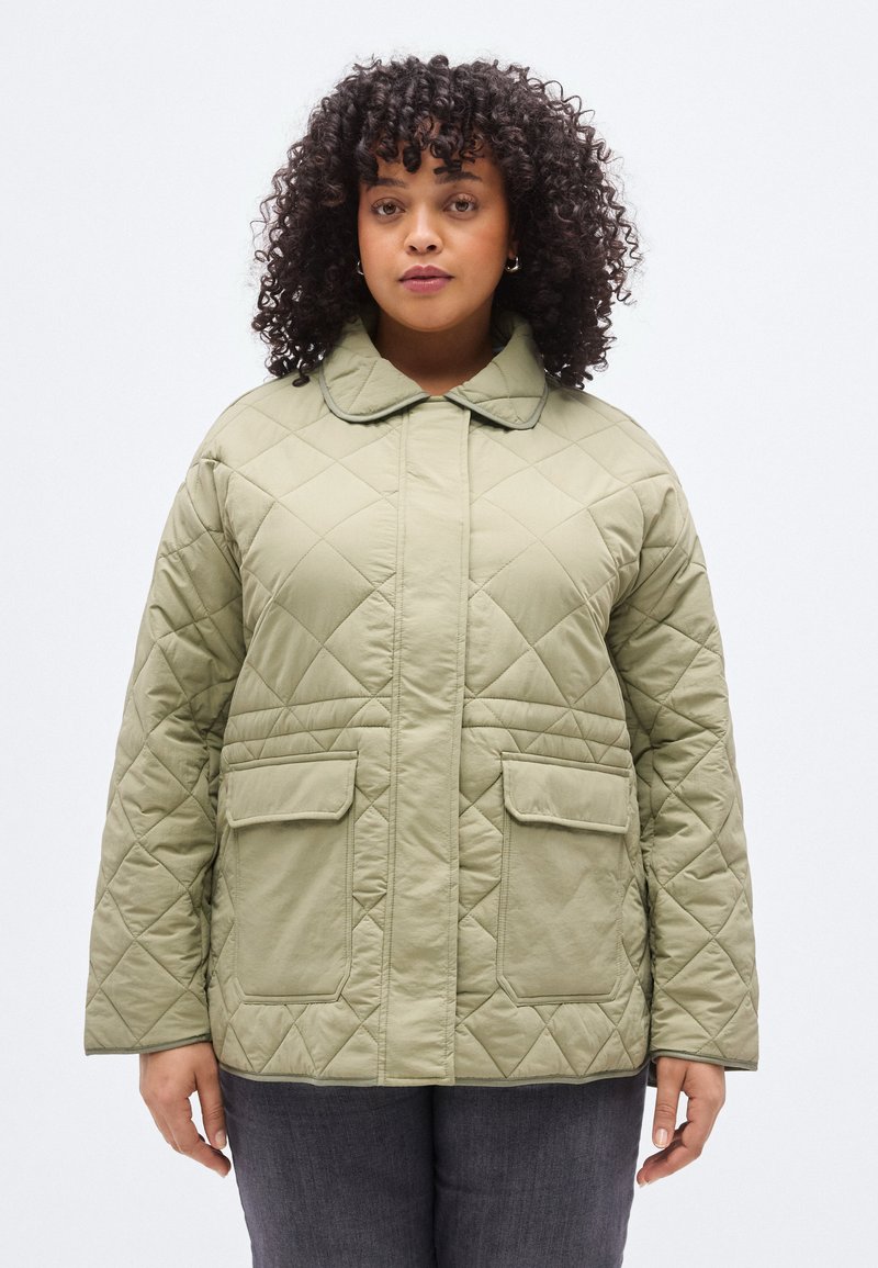 Πράσινο μπουφάν ελιάς με καπιτονέ σχέδιο, μυτερό γιακά, κλείσιμο με κουμπιά μπροστά και δύο μεγάλες εξωτερικές τσέπες. Υφή με διαγώνιο μοτίβο σε σχήμα διαμαντιού.