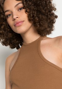 Top croppado castanho com decote halter e gola alta, apresentando cavas largas, uma textura suave e detalhes de costura mínimos.