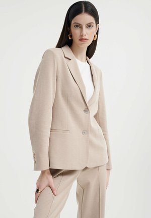 Beige blazer with a tailored design, single-breasted, two buttons, and notched lapels. Features side pockets and textured fabric.