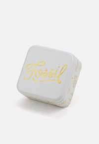 Firkantet metallboks i lys grå med gullskrift "Fossil" på lokket. Har små design langs kantene. Glatt overflate, avrundede hjørner.