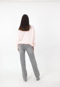 Rosa gestrickter Pullover und graue Bootcut-Hosen. Der Pullover hat eine lockere Passform und überschnittene Schultern; die Hose hat ein klassisches Denim-Design mit Taschen.