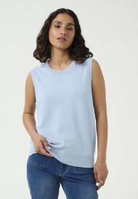 Un pull sans manches bleu clair en tissu doux, avec un col rond et un ourlet légèrement arrondi. Porté avec un jean bleu.