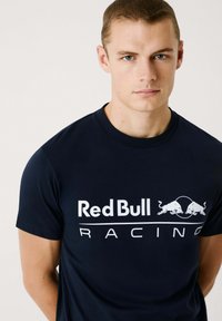 Tamsiai m�ėlyna medvilninė marškinėliai, turintys "Red Bull Racing" logotipą balta spalva. Trumpomis rankovėmis ir apvaliu iškirpimu, lygus paviršius.