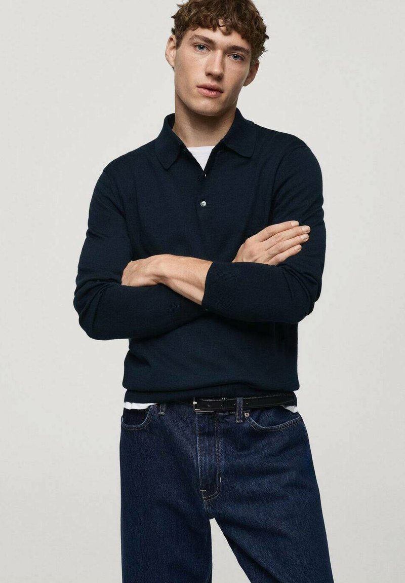 Polo a maniche lunghe blu navy con colletto, abbinato a jeans in denim scuro con vestibilità slim e texture sottile, indossato con una cintura nera.