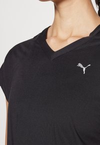Svart V-ringad Puma T-shirt bärs av en person, som visar övre bröstet och Puma-logotypen på vänster sida.