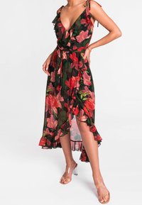 Sorte floral midi kjole med røde og grønne blomster, bølget halsudskæring, bindebånd og asymmetrisk kant. Bæres med klare hælsandaler.